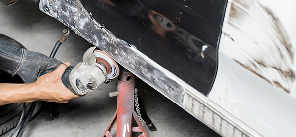 Worker grinding a metal car body panel with a power tool